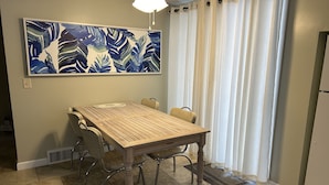 Een eetruimte met een houten tafel en stoelen, een plafondventilator en een groot abstract schilderij aan de muur.