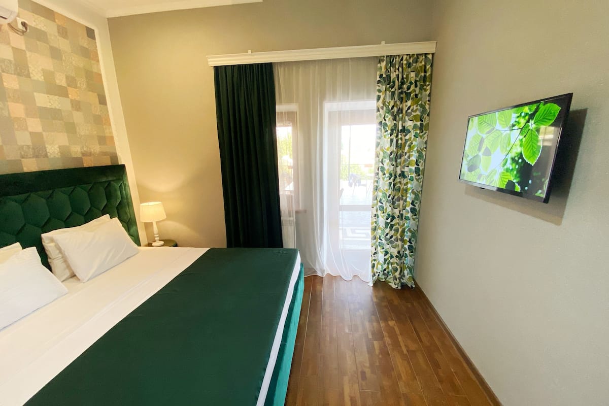 Une chambre d’hôtel avec un lit, une télévision, une fenêtre avec des rideaux et un mur orné d’un motif.
