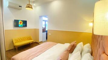 A hotel room with a bed, a yellow sofa, a TV on the wall, and a door leading to a bathroom.