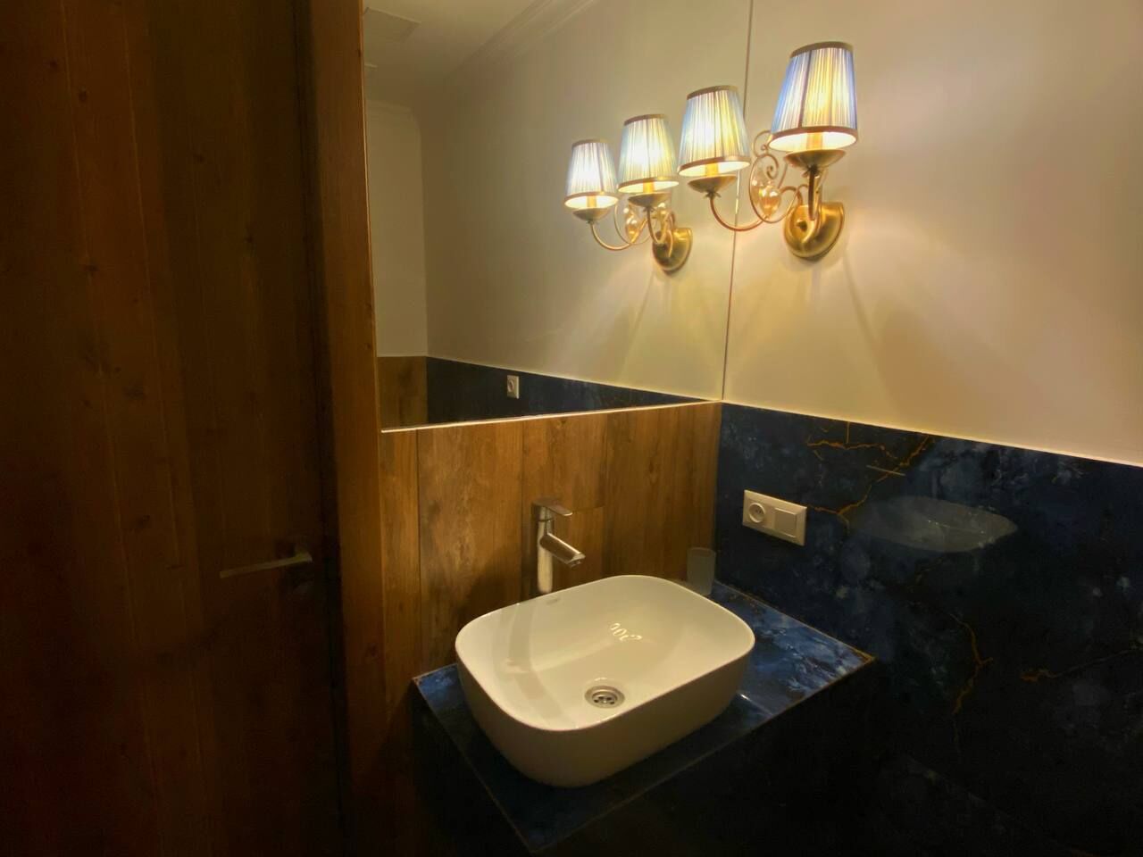 A bathroom with a white sink, wooden paneling, and a blue marble backsplash.