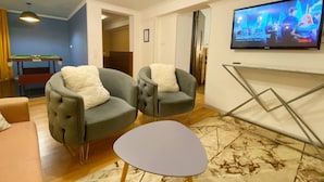Una sala de estar con dos sillones grises, una mesita blanca y un televisor montado en la pared.