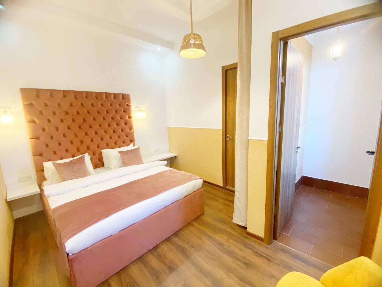 A bedroom with a large bed, a wooden headboard, a bedside table, and a hanging light fixture.