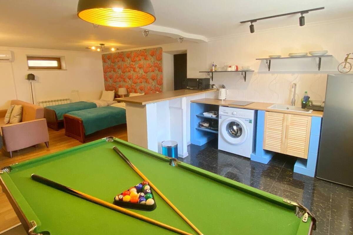 Un espace de vie compact comprenant une table de billard, un canapé, une petite cuisine équipée d’un lave-linge et un vélo.