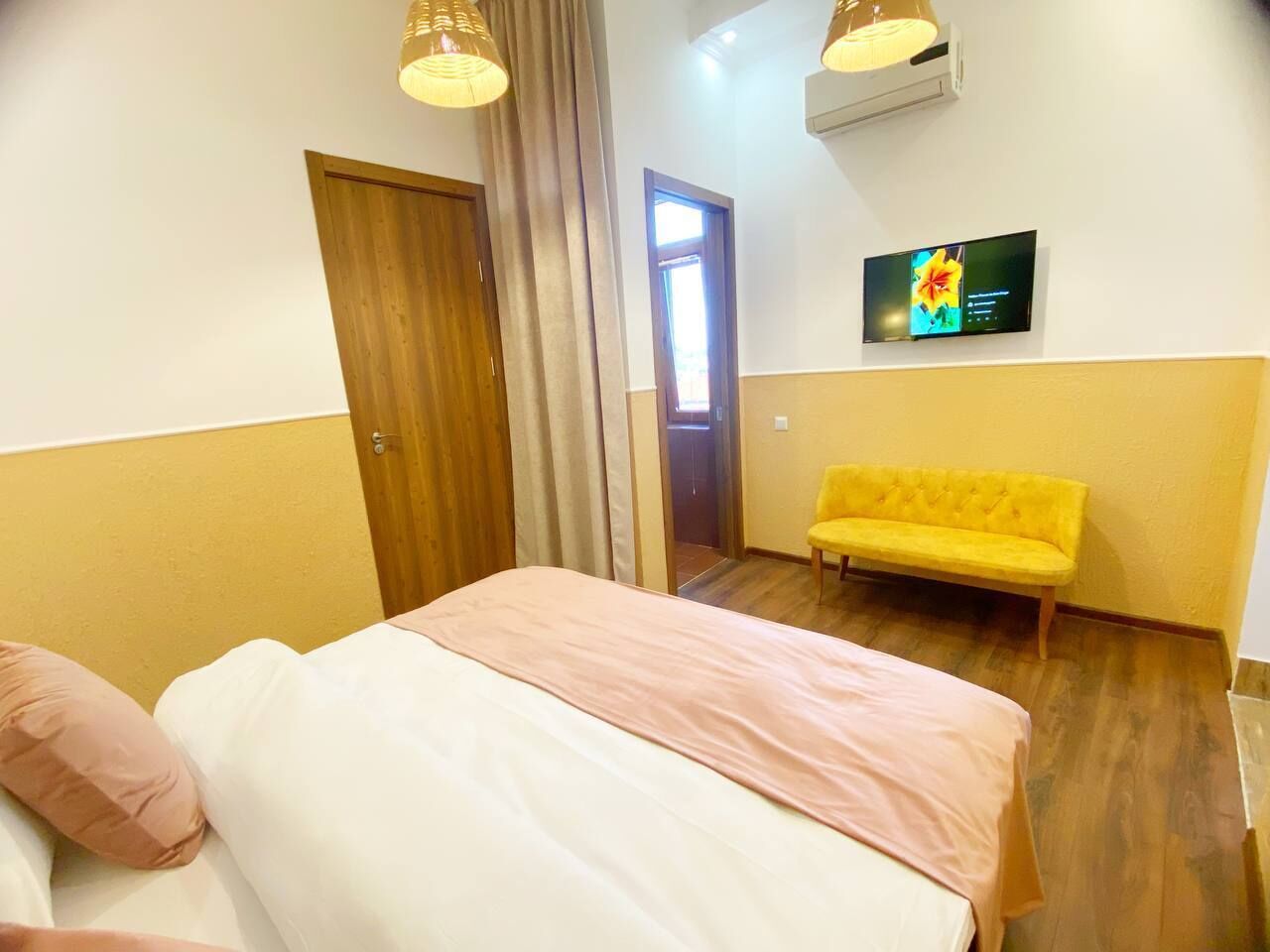 A bedroom with a bed, a yellow sofa, a TV on the wall, and a wooden door.