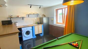 Un espacio habitable pequeño con mesa de billar, lavadora y ventana con cortinas.