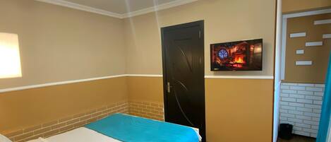 A hotel room with a bed, a TV mounted on the wall, and a door.