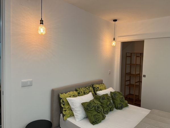 Une chambre à coucher avec un lit, des oreillers verts et blancs, et deux luminaires suspendus.