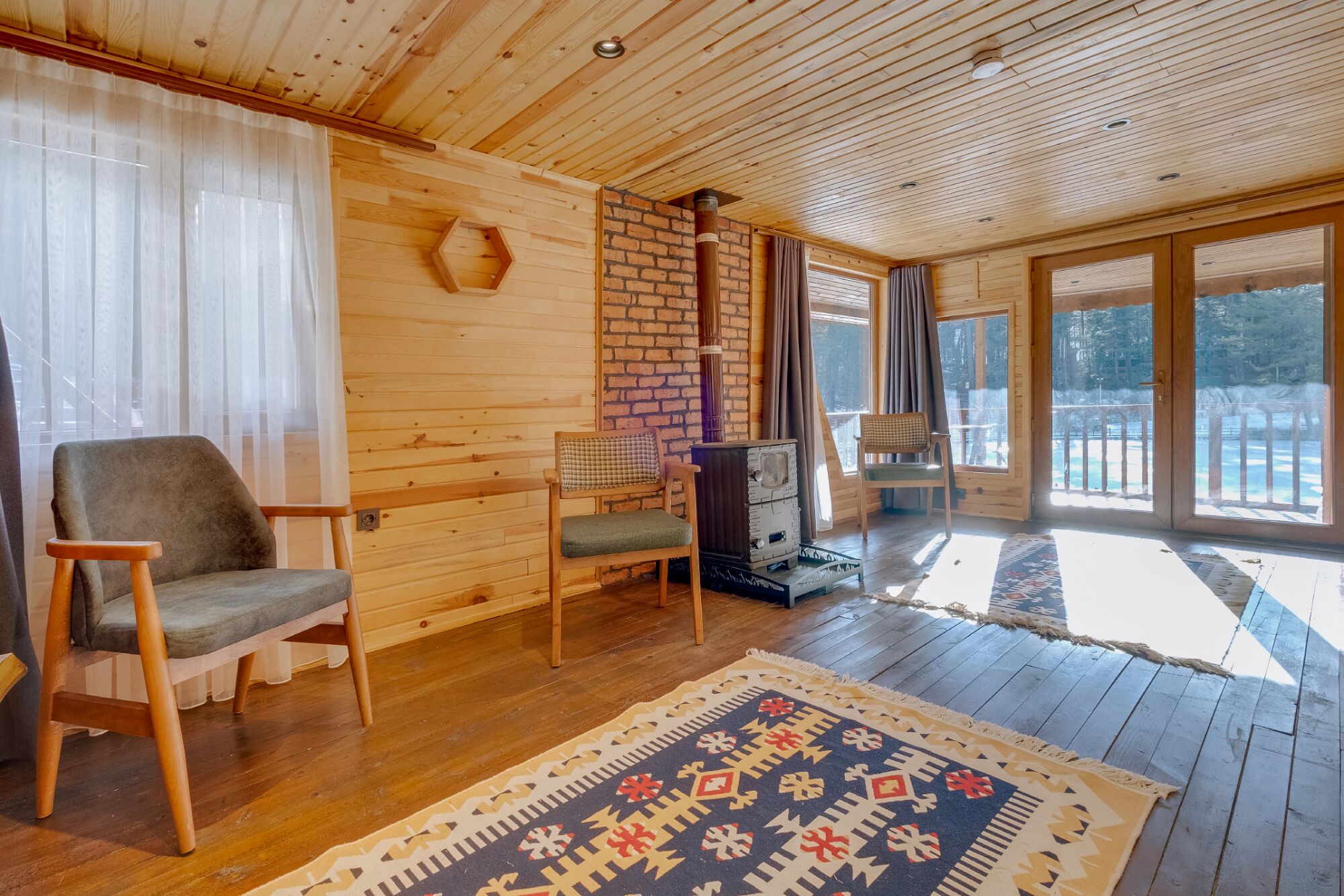 L’intérieur chaleureux d’un chalet avec des murs en bois, une cheminée en briques et une grande fenêtre donnant sur un paysage enneigé.
