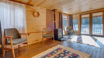 L’intérieur chaleureux d’un chalet avec des murs en bois, une cheminée en briques et une grande fenêtre donnant sur un paysage enneigé.