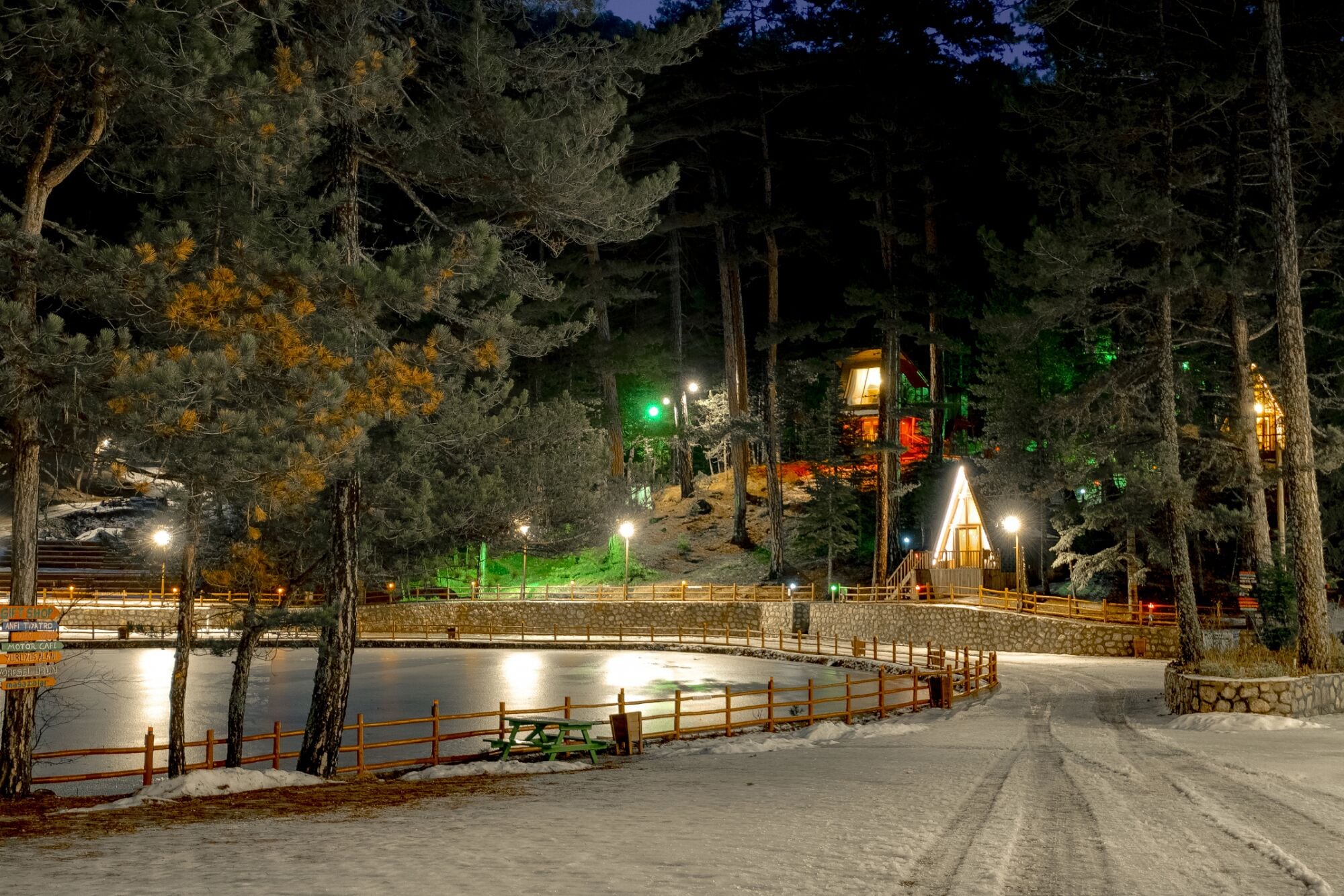 Un espacio exterior cubierto de nieve con una valla de madera, un muro de piedra y un edificio con ventanas iluminadas.