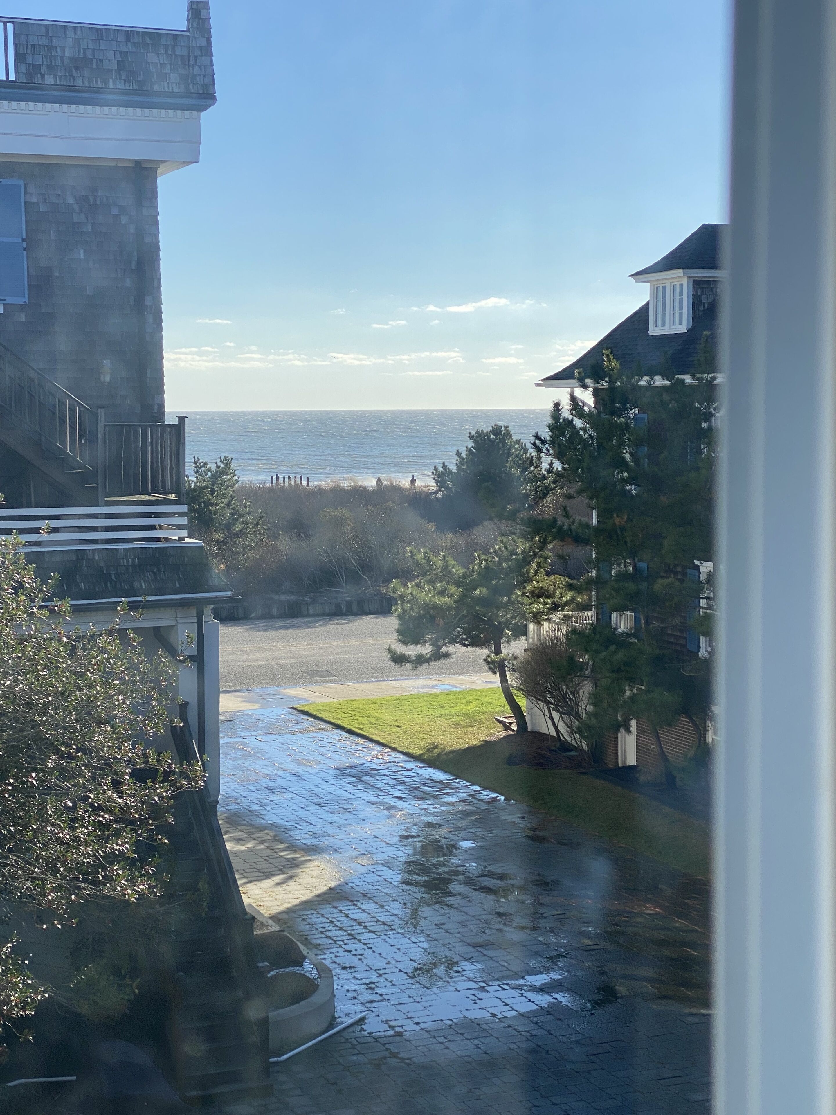 Uitzicht op de kust vanuit een raam, met daarbuiten een verhard gebied, een stukje gras en een waterpartij.