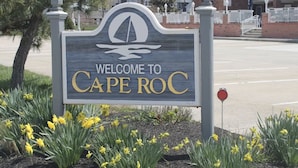 Ein Willkommensschild für Cape Roc mit dem Logo eines Segelboots, umgeben von gelben Narzissen.