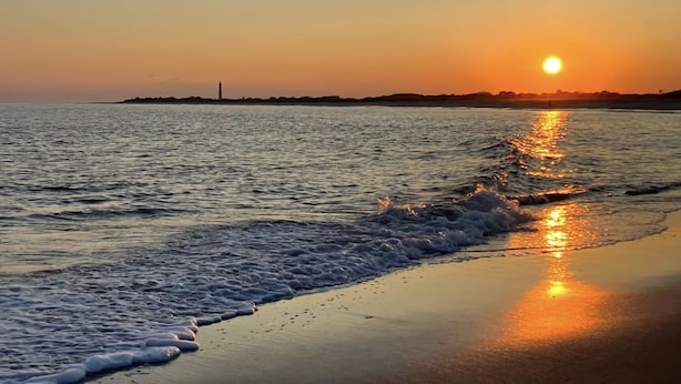 Ein Sonnenuntergang über einem Strand, wo sanfte Wellen am Ufer branden.