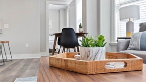 Una sala de estar moderna con una mesa de centro de madera, una maceta de mármol con plantas verdes y un sofá gris con una lámpara.