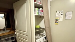 A laundry room with a washing machine, shelves with cleaning supplies, and a door leading to another room.