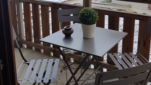 A balcony with a table and chairs, a potted plant, and a view of snow-covered buildings.