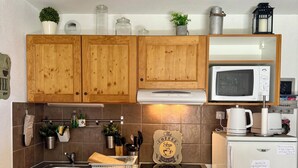 A compact kitchen with wooden cabinets, a microwave, a refrigerator, and a table with a checkered tablecloth.