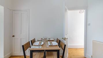 A dining area with a wooden table set for four, surrounded by chairs.