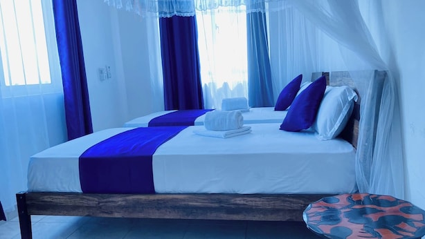 A room with two beds, each with a blue and white bedspread, and a wooden bench. - Apartment Sleeps 6 With Free Parking (Mombasa)