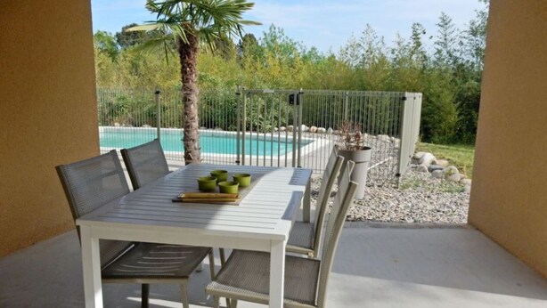 A patio with a white table and chairs, a pool in the background, and a palm tree.