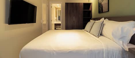 A hotel room with a large bed, a flat-screen TV mounted on the wall, a wardrobe, and a bathroom visible through an open door.