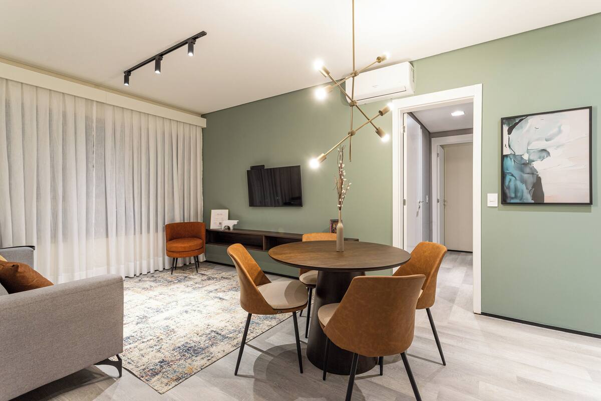 A modern living room with a round dining table, four chairs, a sofa, a TV, and a painting on the wall.