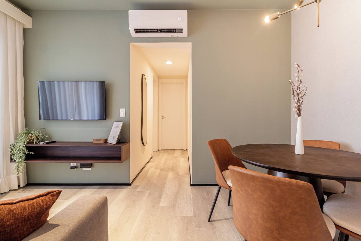 A modern living room with a flat-screen TV, a dining table with chairs, a sofa, and a small plant.