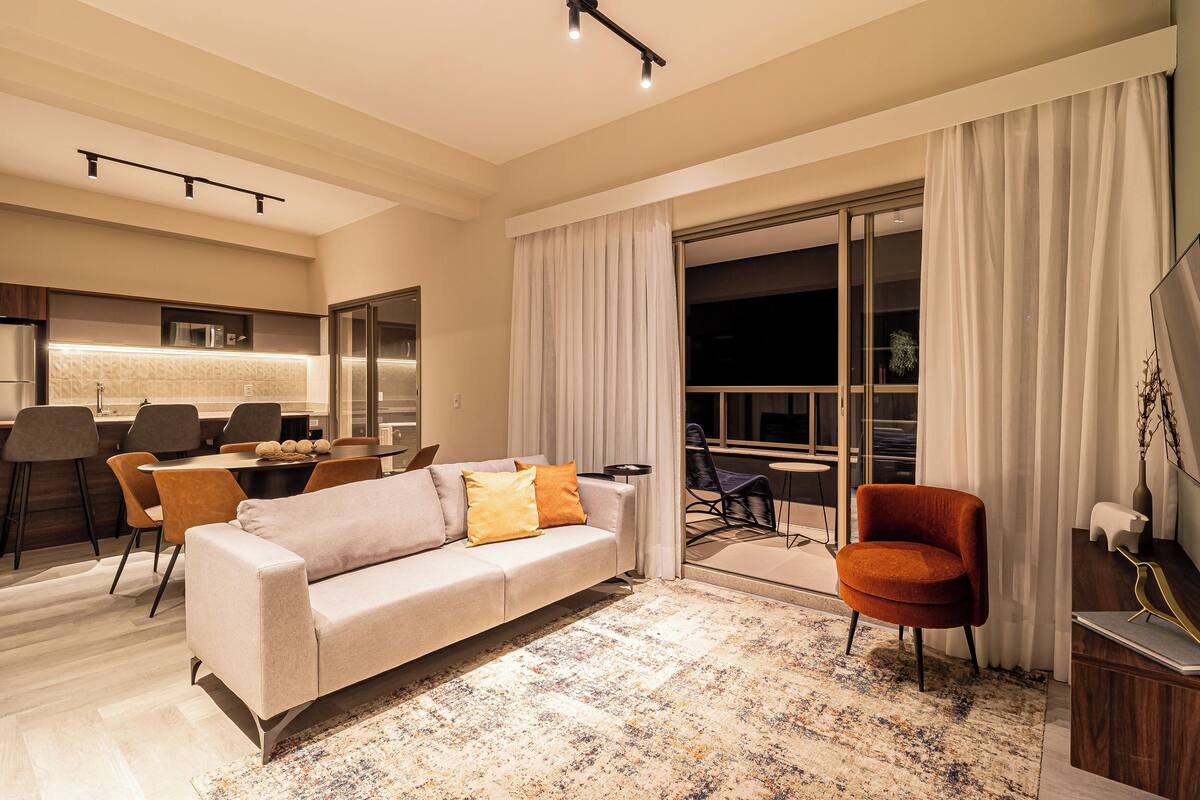 A modern living room with a sofa, armchairs, a dining area, and a large window with curtains.