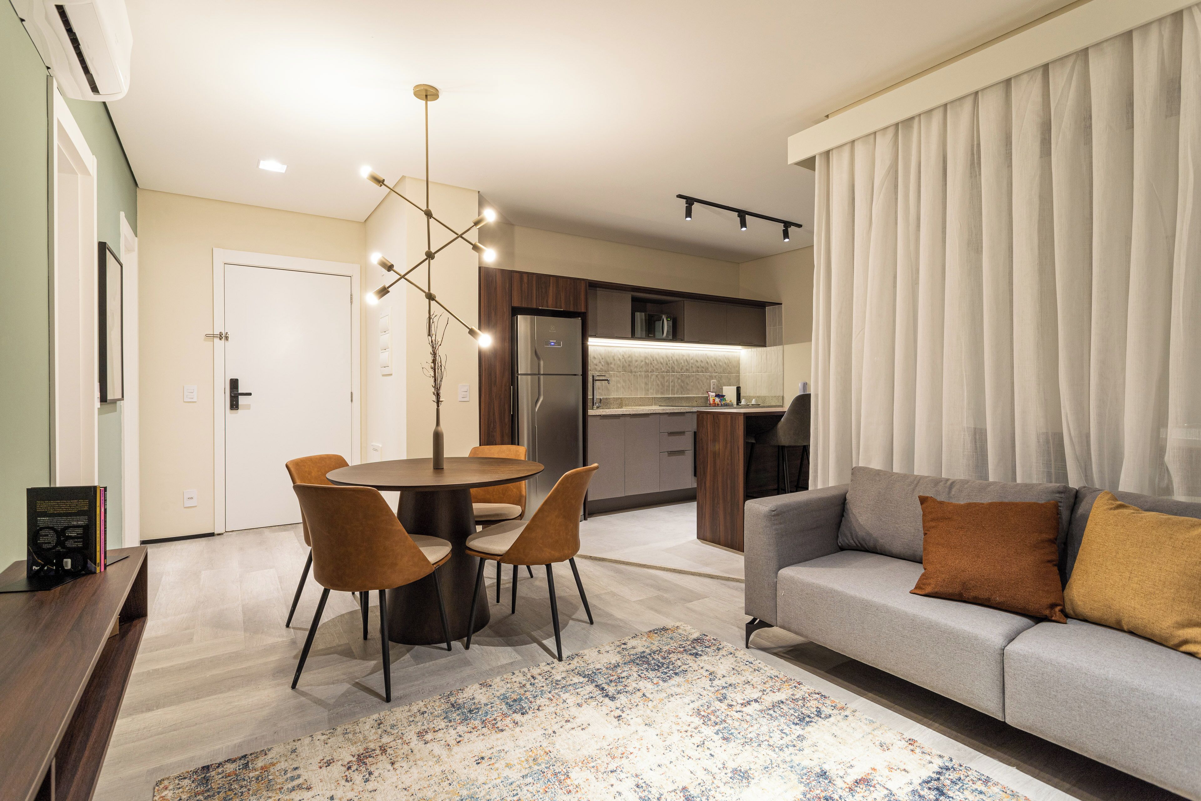 Una sala moderna con un sofá gris, una mesa de comedor con sillas y una cocina al fondo.