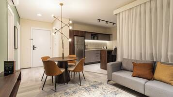 Una sala moderna con un sofá gris, una mesa de comedor con sillas y una cocina al fondo.