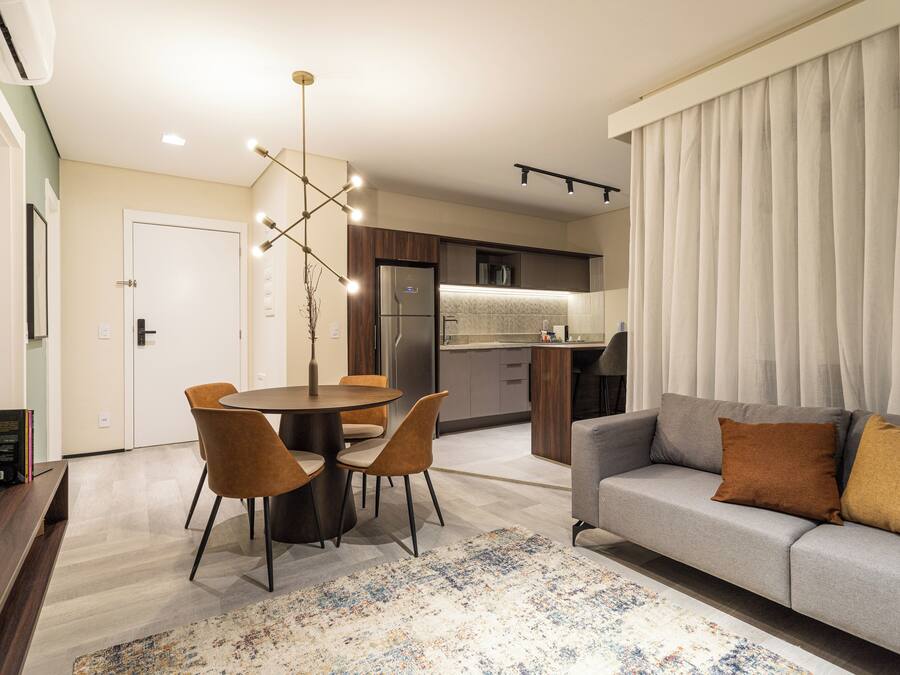 Una sala moderna con un sofá gris, una mesa de comedor con sillas y una cocina al fondo.