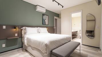 Une chambre moderne avec un grand lit, des tables de chevet, un banc, un miroir fixé au mur et une porte donnant sur une salle de bain.