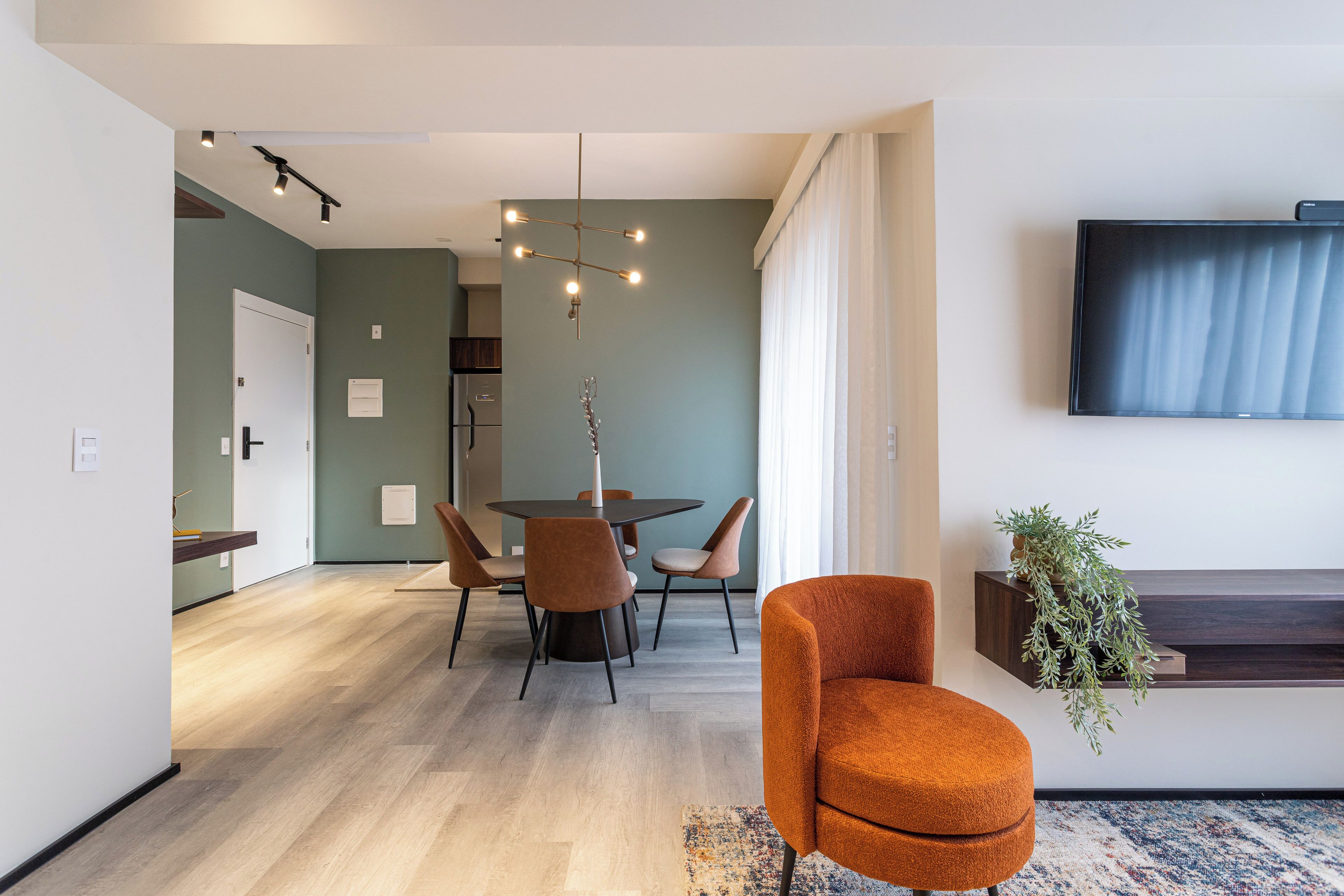Una sala de estar moderna con comedor, televisor montado en la pared y una planta en un estante.