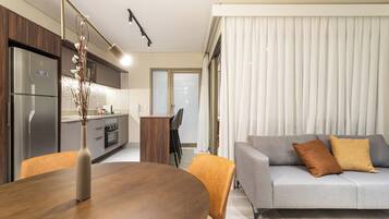 A modern kitchen with a built-in refrigerator, a dining table with chairs, and a grey sofa with cushions.