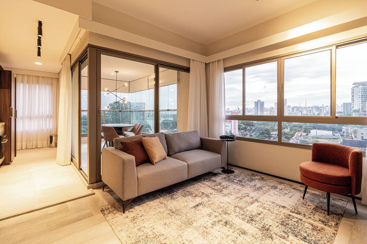A modern living room with a sofa, a chair, and a large window offering a city view.