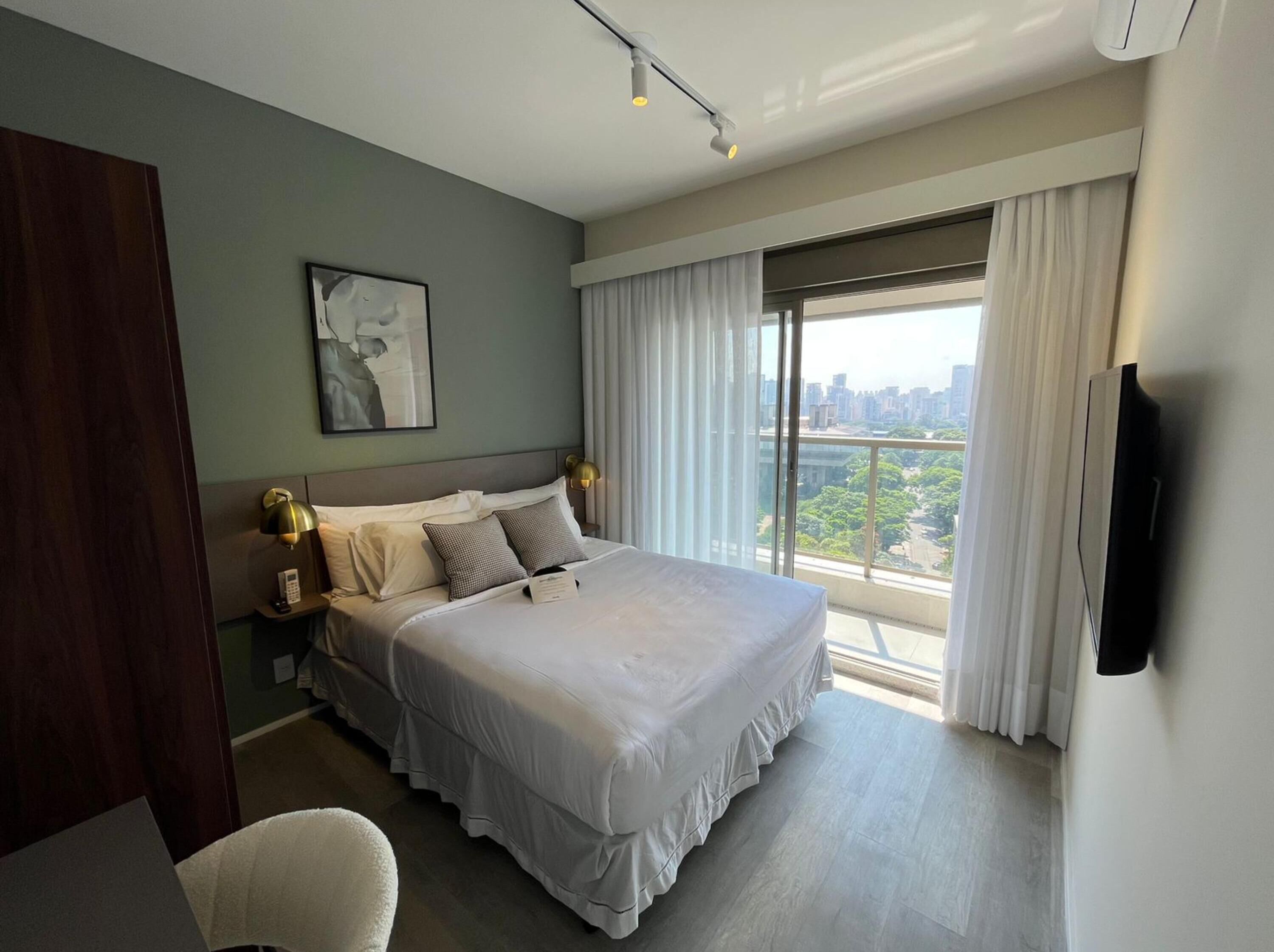 A modern hotel room with a large bed, a city view, and a flat-screen TV.