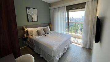 A modern hotel room with a large bed, a city view, and a flat-screen TV.
