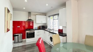 A modern kitchen with white cabinets, a red accent wall, stainless steel appliances, and a glass dining table. - 2 Bed-1 Bath-sleeps 4-parking-pets (High Wycombe)