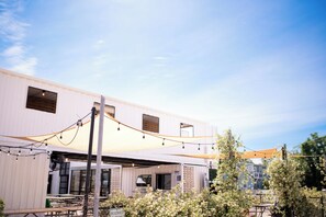 Ein Gebäude mit flachem Dach, großen Fenstern und einer überdachten Terrasse mit Tischen und Stühlen.