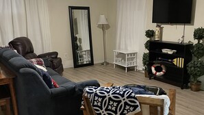 Un salon avec un canapé, une chaise en bois, une lampe sur pied, un téléviseur et une bibliothèque.