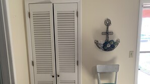 Une pièce avec une porte blanche, une chaise blanche, un paillasson et un élément décoratif mural.