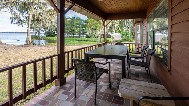 A covered patio with a table and chairs, overlooking a beach and water. - Private Lake View House Rental close to wonderful Big Bass Grill restaurant  (Lake Panasoffkee)
