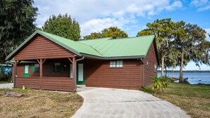 A wooden cabin with a green roof, a porch, and a view of a lake. - Private Lake View House Rental close to wonderful Big Bass Grill restaurant  (Lake Panasoffkee)