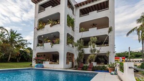 A multi-story building with balconies, a swimming pool, and tropical plants. - Ocean View 2BR | Steps to Beach | Walk to Centro (Bucerías)