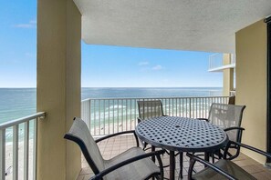 Un balcon avec une table ronde et des chaises, donnant sur une plage et l’océan.