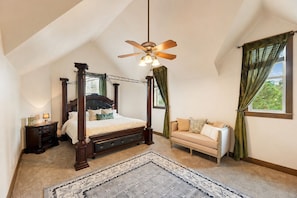 Une chambre à coucher avec un lit à baldaquin, un ventilateur de plafond, un canapé et une vue sur la verdure environnante.