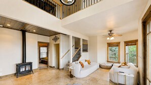 A spacious living area with a high ceiling, a fireplace, a staircase, and large windows. - Granite Pines Chalet (Prescott)