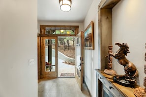 A hallway with a wooden door leading to a garden, a statue on a table, and a framed picture on the wall.