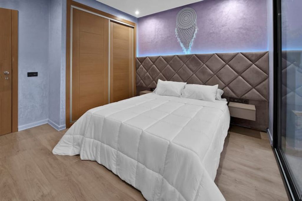 A bedroom with a large bed, a wooden wardrobe, and a wall with a geometric design.
