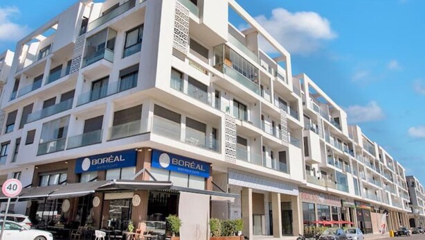 A multi-story building with a modern architectural design, featuring a storefront with a 'Boreal' sign, outdoor seating, and a clear blue sky in the background.